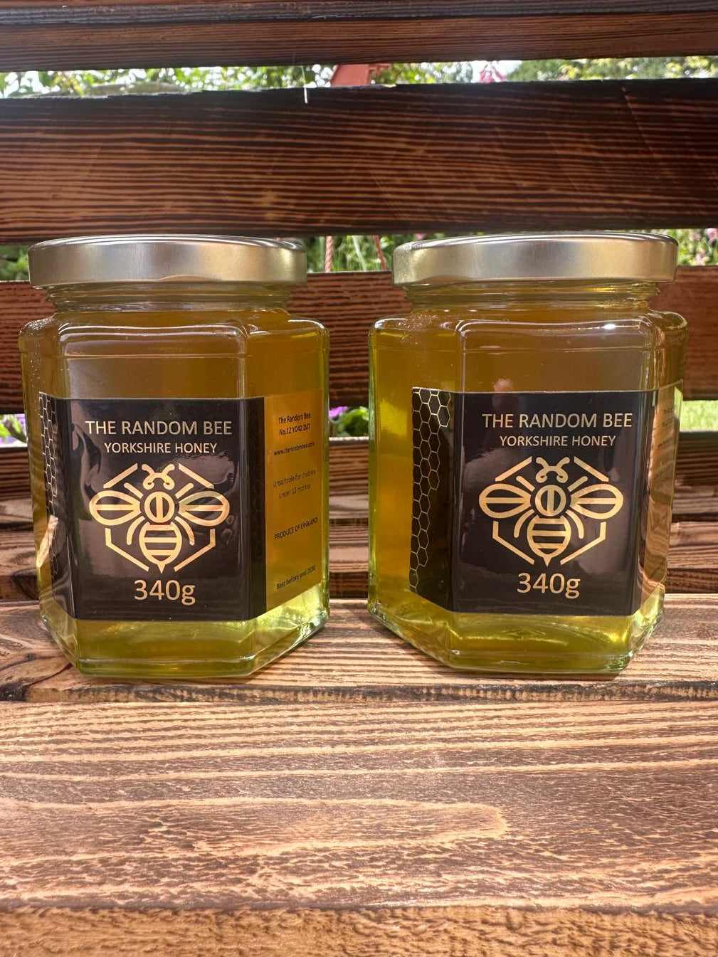 Two jars of 'The Random Bee Yorkshire Honey' 340g on a wooden surface with a blurred natural background.