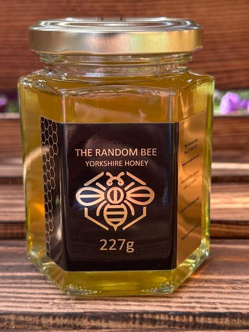 Jar of honey from 'The Random Bee' 227g on a wooden surface with blurred natural background